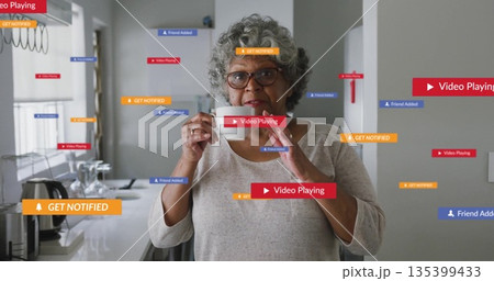 Woman wearing gray shirt tasting with spoon in kitchen, with floating colored notification banners 135399433