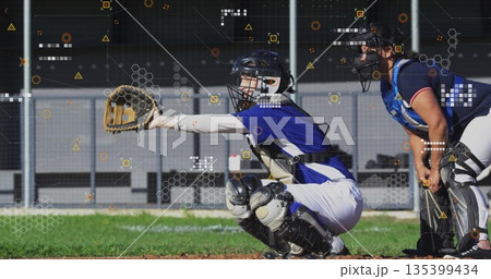 Squatting female catcher extending glove at ballpark, with teammate watching and digital overlays 135399434