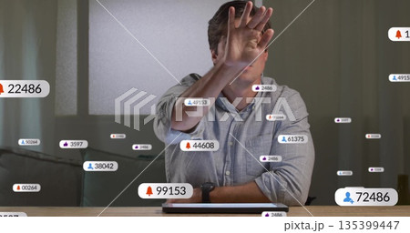 Man wearing shirt smartwatch shielding face in home office, floating alert badges, laptop pressure 135399447