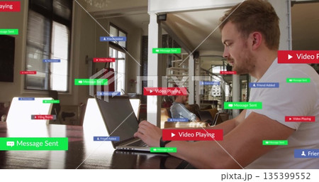 Typing man in white T-shirt working on laptop at table in living room, with floating labels Typing man in white T-shirt working on laptop at table in living room, with floating labels 135399552