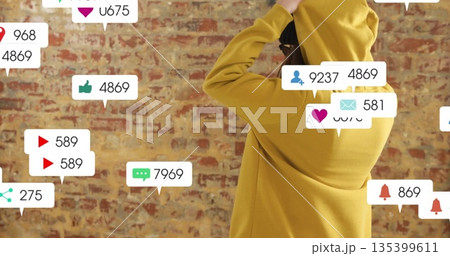 Lifting yellow hoodie over head, woman standing by brick wall, with social icons, copy space 135399611
