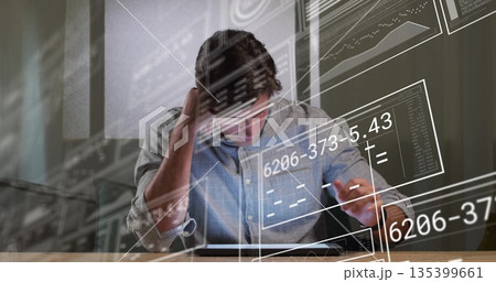 Man in blue shirt studying tablet with virtual equations and charts at desk in modern office 135399661