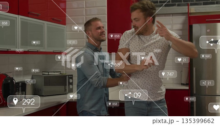 Interacting two men checking floating social media icons in kitchen with red cabinets and fridge 135399662