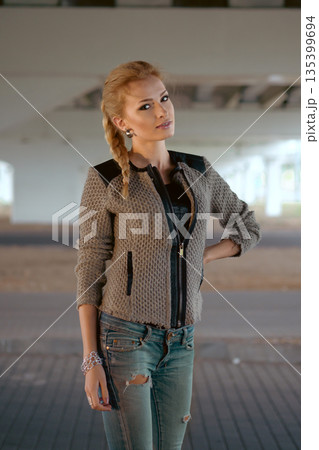 Model poses in urban setting under bridge while wearing denim jeans and a stylish jacket 135399694