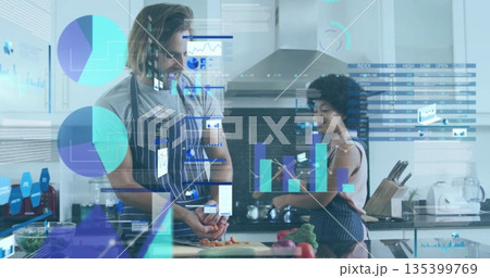 Couple in aprons chopping carrots and consulting smartphone at kitchen island with floating data Couple in aprons chopping carrots and consulting smartphone at kitchen island with floating data 135399769
