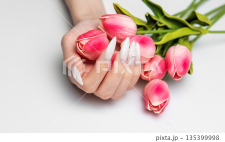 Hand holding pink tulips displaying long white nails Hand holding pink tulips displaying long white nails 135399998