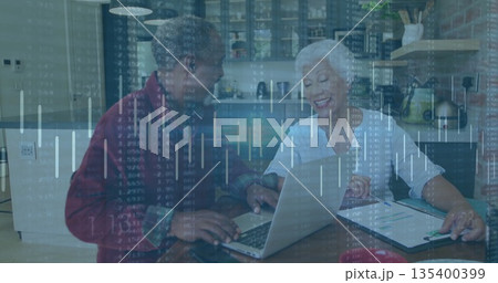 Senior couple reviewing financial data on silver laptop in modern kitchen, with clipboard and pen Senior couple reviewing financial data on silver laptop in modern kitchen, with clipboard and pen 135400399