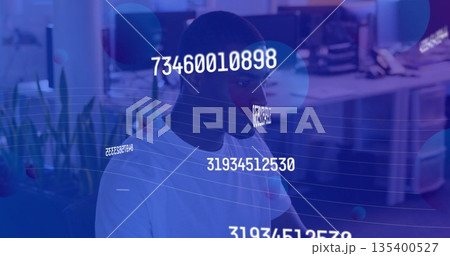 Working African American man analyzing monitor data in modern office, with numeric overlays Working African American man analyzing monitor data in modern office, with numeric overlays 135400527