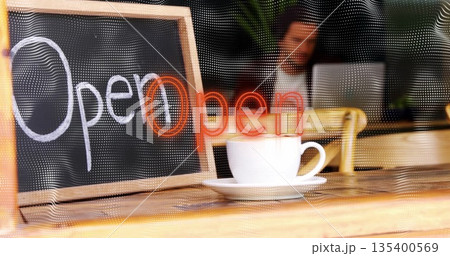Displaying chalkboard sign leaning on café counter, reflecting neon Open with coffee cup, laptop 135400569