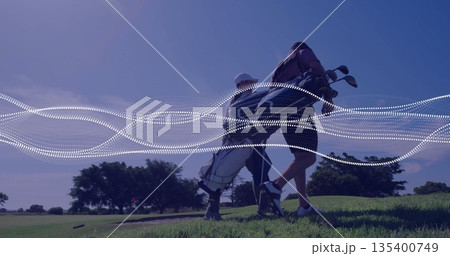 Walking two male golfers carrying golf bags with clubs uphill on sunlit fairway with dotted overlay Walking two male golfers carrying golf bags with clubs uphill on sunlit fairway with dotted overlay 135400749