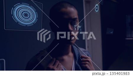 Gripping backpack Asian male in denim shirt examining UI panels in dim corridor, with smartphone 135401983