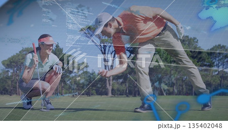 Kneeling and crouching couple in golf attire examining putt line on golf green, digital overlays 135402048