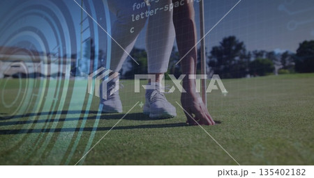 Bending female golfer retrieving golf ball on putting green, with flagstick and digital overlay 135402182