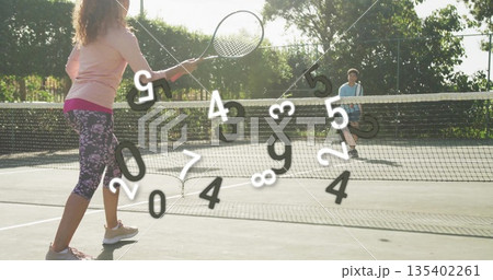 Woman in purple leggings swinging tennis racket near net on park tennis court, with man 135402261