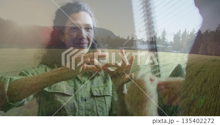 Two women with one in green shirt signing messages indoors, window blinds revealing farmhouse hills 135402272