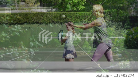 Tossing tennis ball mother in sportswear coaching daughter on home court with racket net plants Tossing tennis ball mother in sportswear coaching daughter on home court with racket net plants 135402274