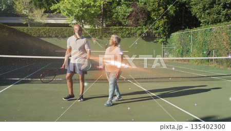 Walking African American man and senior woman on private tennis court with net, carrying rackets Walking African American man and senior woman on private tennis court with net, carrying rackets 135402300