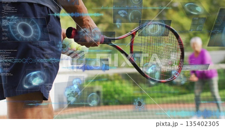 Swinging senior man gripping tennis racket on clay court with net, tennis ball, digital HUD 135402305