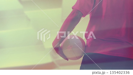 Standing woman in red jersey black shorts holding volleyball at gym under pink lighting, copy space Standing woman in red jersey black shorts holding volleyball at gym under pink lighting, copy space 135402336