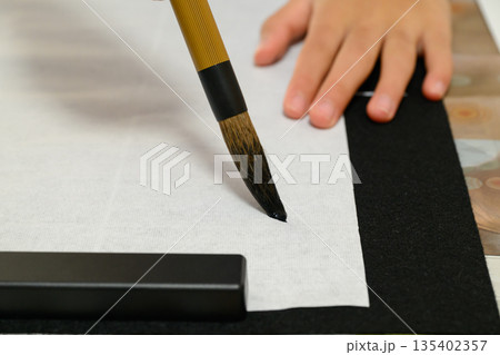 半紙に筆を下ろす子供の手元と書道道具 半紙に筆を下ろす子供の手元と書道道具 135402357
