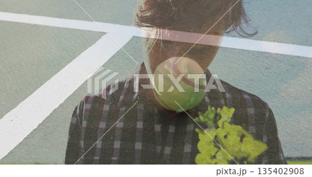 Standing man in checkered shirt showing tennis ball and yellow flower overlays on green court lines Standing man in checkered shirt showing tennis ball and yellow flower overlays on green court lines 135402908