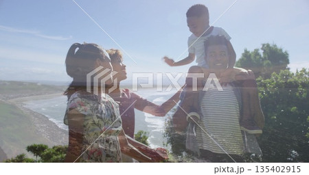Walking family carrying son on shoulders along coastal bluff path, with ocean view, floral sundress 135402915