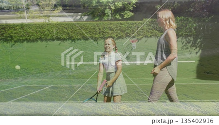 Practicing mother coaching daughter on grass court wearing grey top, skirt, with racket, ball, net 135402916
