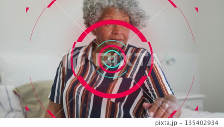 Senior woman wearing striped shirt using AR interface with pillow, blanket, table in bedroom 135402934