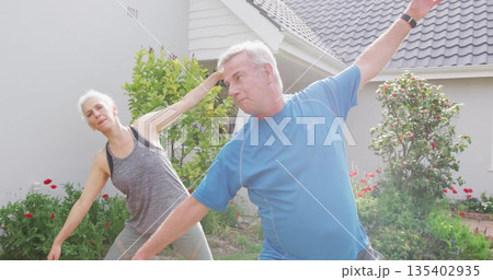 Stretching couple wearing athletic wear doing side stretches on grass lawn, with fitness tracker Stretching couple wearing athletic wear doing side stretches on grass lawn, with fitness tracker 135402935