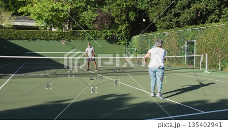Couple playing tennis on outdoor tennis court, with rackets, ball, net, hoop and boundary lines Couple playing tennis on outdoor tennis court, with rackets, ball, net, hoop and boundary lines 135402941