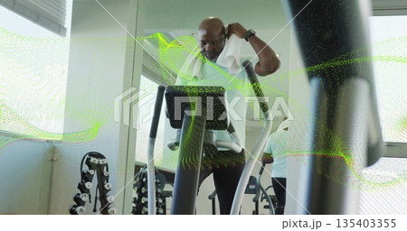 Senior man pulling white workout towel on treadmill in fitness center, with dumbbell rack Senior man pulling white workout towel on treadmill in fitness center, with dumbbell rack 135403355