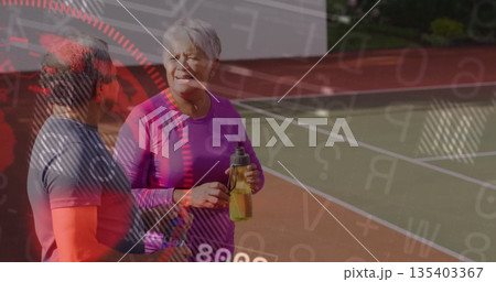 Chatting senior pair in sportswear on tennis court, with white boundary lines and water bottle 135403367