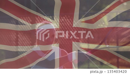 Swinging female tennis athlete holding racket on outdoor hardcourt, with Union Jack overlay 135403420