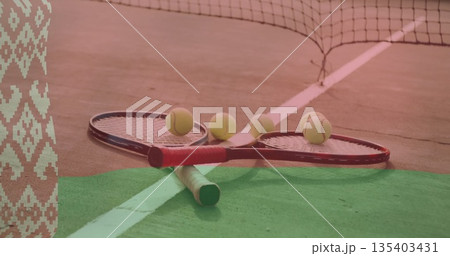 Lying crossed tennis rackets with five yellow balls on outdoor hard court, with net, boundary lines 135403431