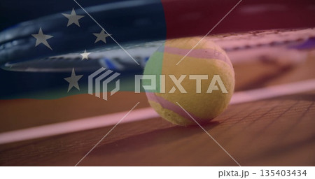 Hovering tennis racket strings pressing down on tennis ball on hard court, with flag overlay 135403434