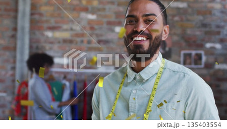 Smiling man wearing green top and measuring tape standing in studio, with rack, photos and confetti 135403554