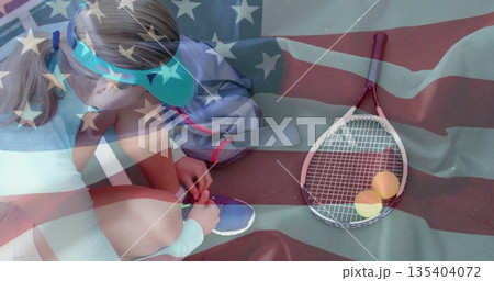Kneeling tennis player tying shoelaces on tennis court, with racket, balls, backpack, copy space 135404072
