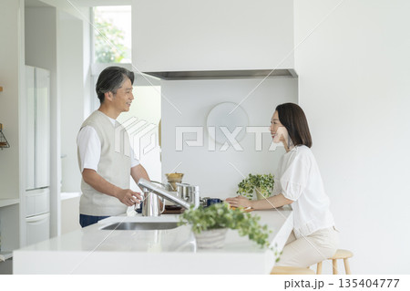 キッチンのカウンター越しに話をする笑顔の50代の夫婦 キッチンのカウンター越しに話をする笑顔の50代の夫婦 135404777