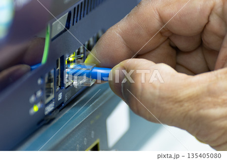 Close-up of a hand plugging a blue ethernet cable into a network switch or router. Concept data connection, internet technology, and IT infrastructure. 135405080