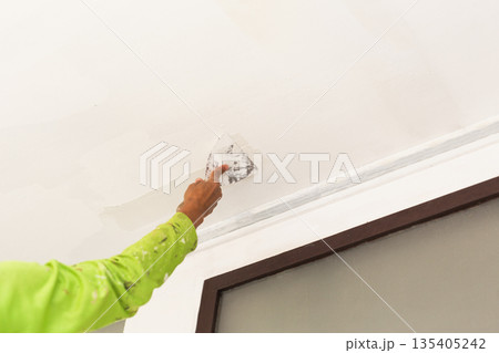 A worker applying plaster with a putty knife to smooth a ceiling surface. A worker applying plaster with a putty knife to smooth a ceiling surface. 135405242
