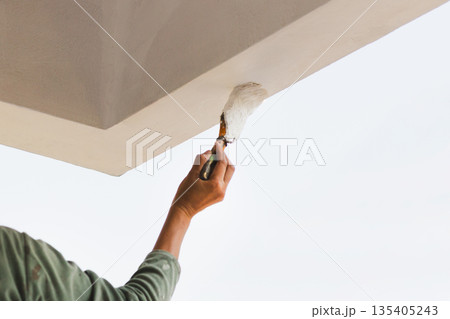 A close up of person painting an exterior ceiling edge with a brush. A close up of person painting an exterior ceiling edge with a brush. 135405243