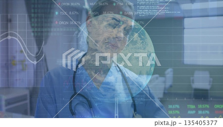 Standing medic in blue scrubs and stethoscope reviewing charts and globe at consultation desk Standing medic in blue scrubs and stethoscope reviewing charts and globe at consultation desk 135405377