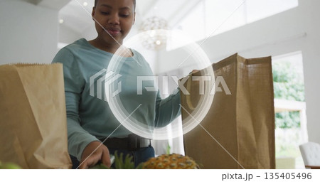 Unpacking woman wearing teal top unloading groceries at marble island, pineapple and leafy greens 135405496