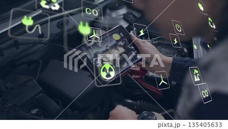 Examining mechanic's hands holding tablet computer at auto repair workshop bay, with energy icons Examining mechanic's hands holding tablet computer at auto repair workshop bay, with energy icons 135405633