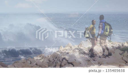 Holding hands couple standing on rocky coastal outcrop, with hiking backpacks and boots, copy space Holding hands couple standing on rocky coastal outcrop, with hiking backpacks and boots, copy space 135405638