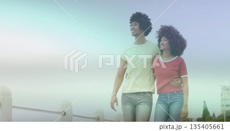 Walking couple wearing T-shirt and jeans strolling along waterfront promenade with metal railing 135405661