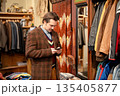 Elegant man in classy blazer checking smartphone during shopping in vintage men's clothing store. 135405877