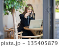 Relaxed woman freelancer enjoying conversation on smartphone while working with laptop in cafe. 135405879