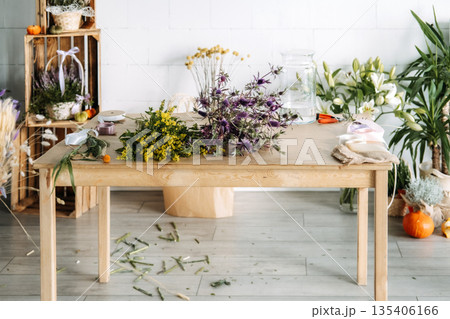 Dried flowers and sea holly stems lay on wooden table in bright studio. Florist workspace, zero waste event planning, eco friendly floral studio. Dried flowers and sea holly stems lay on wooden table in bright studio. Florist workspace, zero waste event planning, eco friendly floral studio. 135406166