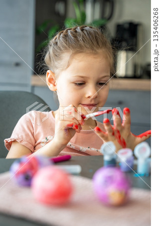Little girl painting her hand with red paint while decorating Easter eggs at home. Creative Easter activity, childhood curiosity and playful holiday preparation indoors. Little girl painting her hand with red paint while decorating Easter eggs at home. Creative Easter activity, childhood curiosity and playful holiday preparation indoors. 135406268